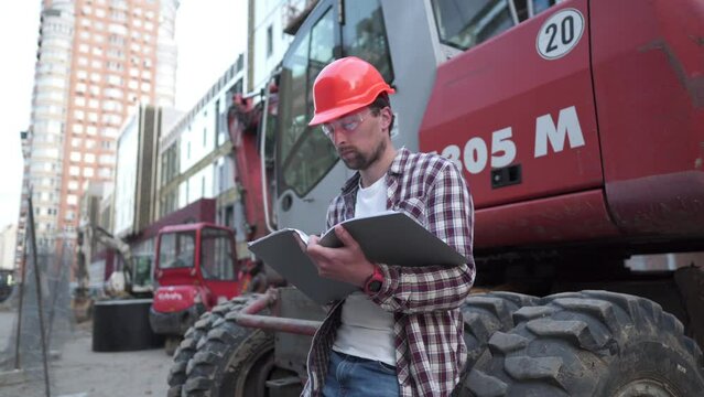 Industrial worker reviewing plans. Construction worker holding project documents near a bulldozer at a construction site. Construction manager, engineer explore construction documentation.