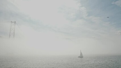 Sailboat sails the sea in dense fog - a plane flies in the sky