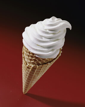 Ice cream cone with soft serve vanilla ice cream on a waffle cone standing up on a red background