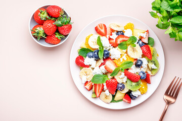 Sweet fruit berry salad with strawberries, blueberries, banana, soft cheese and mint leaves, pink background, top view