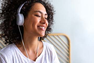 Happy young African American latina woman listening to music using white headphones at home...