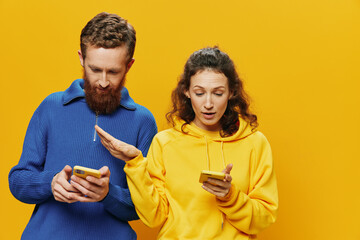 Woman man cheerful couple with phones in hand social networking and communication crooked smile fun and fight, in yellow background. The concept of real family relationships, freelancers, work online.