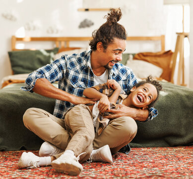 Happy afro american family father and son laughing and playing while sitting on bed at home.