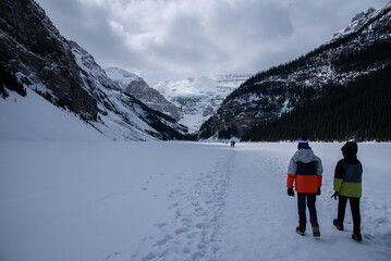 Fototapeta na wymiar Two kids walking on a Frozen Lake Louise enjoying Canadian winter months. Wonderful winter landscapes of Canada. 
