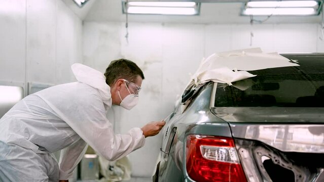 Man mechanic, standing holding sheet thin steel sheet, inspecting car's paint, checking if car color customer's desired color match or not spray equally or not, before calling customer pick up car