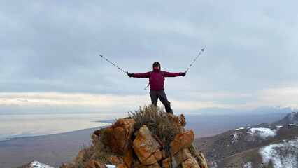 Lonely tourist stands on top of a mountain with trekking poles raised up. View from the height of...