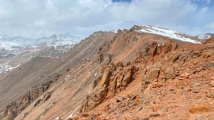 Amazing mountain landscape. Panorama of red rocky cliffs and snow-capped mountains. Blue sky and white clouds. The amazing nature of Kyrgyzstan.