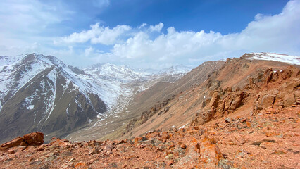 Panorama of red rocky cliffs and snow-capped mountains. Blue sky and white clouds. The amazing nature of Kyrgyzstan. Amazing mountain landscape.