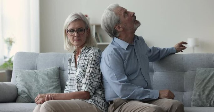 Aged married couple arguing at home, old angry man express discontent, seated on sofa with sad silent spouse. Upset mature woman listening irritated husband makes claims to wife. Abusive Generative AI