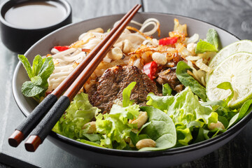 Bowl of delicious mixed beef noodle salad Pho Tron closeup on the wooden table. Horizontal