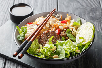 Vietnamese beef rice noodles salad with leafy vegetables, nuts and onions close-up in a bowl on a wooden table. horizontal