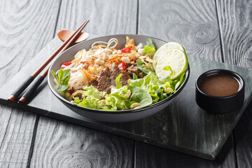 Pho Bo Tron Vietnamese beef rice noodles salad close-up in a bowl on a wooden table. horizontal