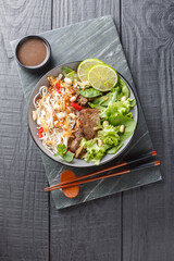 Bowl of delicious mixed beef noodle salad Pho Tron closeup on the wooden table. Vertical top view...