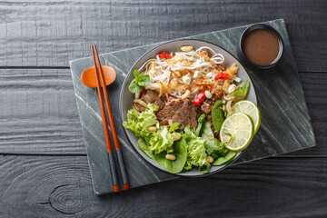 Pho Bo Tron Vietnamese beef rice noodles salad close-up in a bowl on a wooden table. horizontal top...