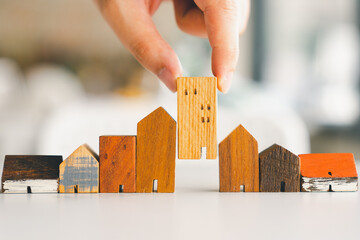 Hand choosing mini wood house model from model and row of coin money on wood table, selective...