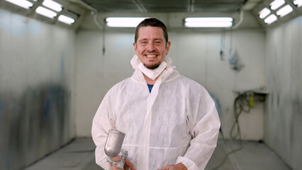 Fototapeta premium Caucasian Man mechanic, Mechanic holding car paint sprayer, Wearing hat attached PPE suit, wearing mask glasses for safety, before painting car in non-ventilated room for consistent car paint.
