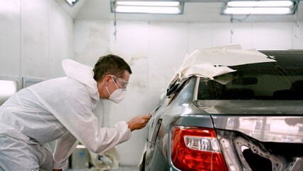 Man mechanic, standing holding sheet thin steel sheet, inspecting car's paint, checking if car color customer's desired color match or not spray equally or not, before calling customer pick up car