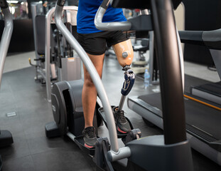 Fototapeta na wymiar Low angle view at woman with prosthetic leg use exercise machine at fitness gym