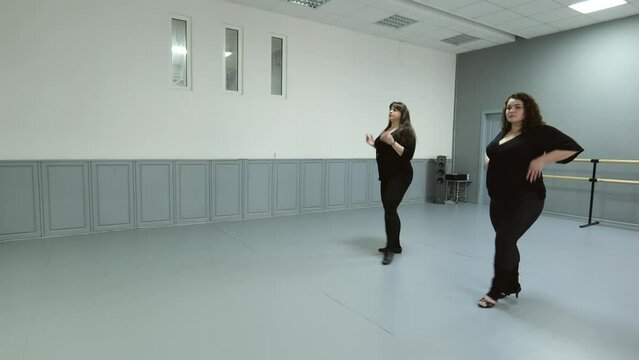 Two fat women in dark clothes are dancing in the hall. woman dance