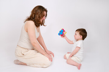 Happy baby with mother play educational toys on studio white background. Portrait of a smiling child with mom and playing while sitting on the floor. Kid about two years old (one year nine months)