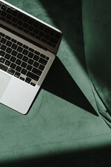 Flatlay laptop computer and gentle sunlight shadow on green velour sofa. Top view minimalist...