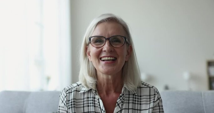 Portrait of senior woman sit on sofa look at camera talk on videoconference with relatives or friends use modern app, laugh, share news, gesturing, enjoy distancing communication, close up