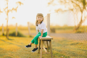 relaxing style of asian baby cute girl sit on the bench wood on a the outdoor grass ground with happy time on evening time