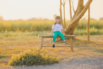 relaxing style in Alone Emotional of asian baby cute girl sit on the bench wood on a the outdoor grass ground with happy time on evening time