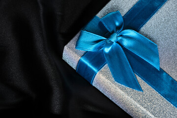 Silver gift box with blue bow background black silk fabric.