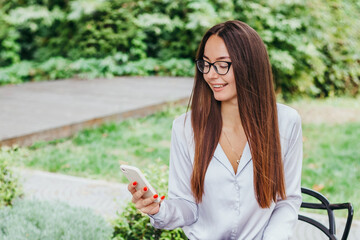 A young brunette woman in glasses sits at a table in a cafe and works at a laptop