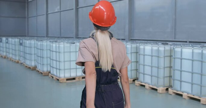 Factory worker are pulling cart at warehouse with big bottles, conteiners Young Caucasian woman push hand pallet stacker. . Slow Motion back view