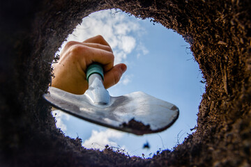Close-up of man hand digging garden pits for planting plants. View from a freshly dug pit full of clay. View from below.