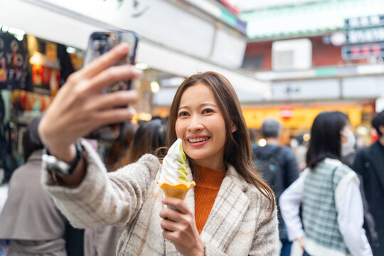 Asian woman using mobile phone taking selfie together during eating ice cream at Asakusa district, Tokyo, Japan. Attractive girl enjoy and fun outdoor lifestyle travel city street on holiday vacation.