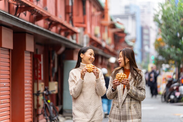 Happy Asian woman friends eating Japanese sweet bread together during travel at Asakusa, Tokyo,...