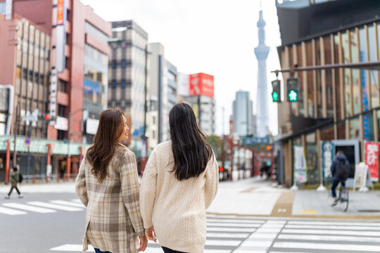Asian woman friends crossing street crosswalk with crowd of people during travel together at Asakusa, Tokyo, Japan in autumn. Attractive girl enjoy urban outdoor lifestyle travel on holiday vacation.