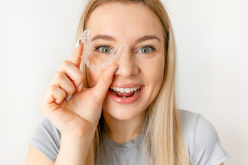 Cheerful girl holding dental aligner orthodontic to teeth correction with happy face near eye