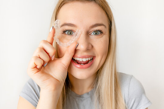 Cheerful girl holding dental aligner orthodontic to teeth correction with happy face near eye
