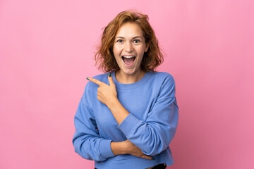 Obraz premium Young Georgian woman isolated on pink background surprised and pointing side
