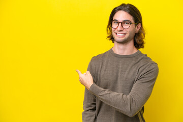 Caucasian handsome man isolated on yellow background pointing back