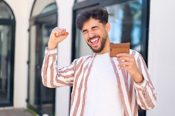 Handsome Arab man at outdoors holding a wallet and celebrating a victory