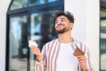 Handsome Arab man at outdoors holding wallet with money and looking it