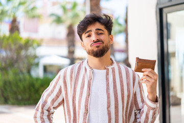 Handsome Arab man holding a wallet at outdoors with sad expression