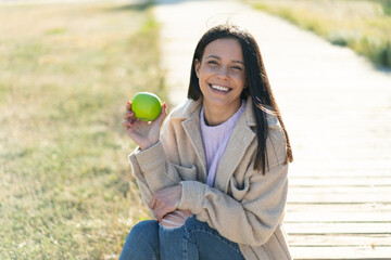 Young woman at outdoors holding an apple with happy expression