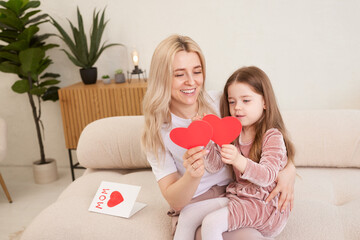 Happy Mother's Day! The child's daughter congratulates her mother and gives her flowers tulips and a card. Mom and girl smile and hug. Family vacation and togetherness.