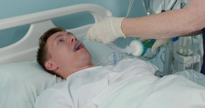 man put tubes into patient's mouth, while performing surgery. Nurse works with ventilator while treating man with coronavirus. After operation, patient is connected to artificial respiration apparatus