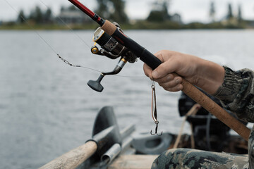 Fisherman holding spinning rod with fishing reel and fishing lure in hand in boat, close up