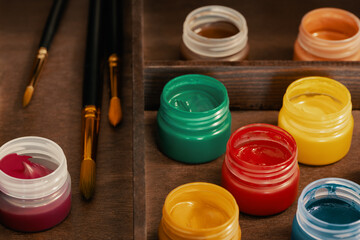 Artistic gouache and paintbrushes in wooden easel box, high angle shot. Eight open bottles of...