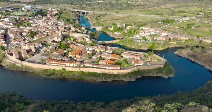 Aerial view of Buitrago del Lozoya, a well preserved historic village near Madrid, surrounded by the Lozoya river, with the Guadarrama mountain chain and reservoir in the background. Long exposure.