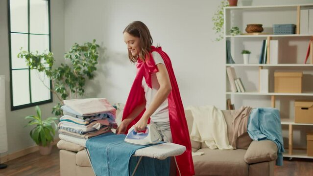 Happy Woman Housewife in Super Hero Cape Dancing While Ironing Clothes at Home.Creativity and Imagination:Using Homework as a Platform For Creative Self-realization and Development of the Imagination.