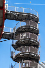 Circular iron staircase for fire escape outside a modern metal industrial building fence in the open air.